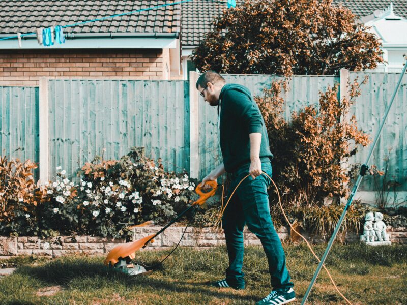 man holding orange electric grass cutter on lawn